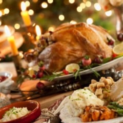 Mesa de ceia de Natal com peru assado, pur&ecirc;, farofa, legumes e decora&ccedil;&atilde;o com velas e luzes natalinas.