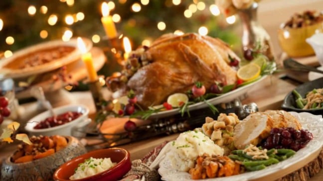 Mesa de ceia de Natal com peru assado, purê, farofa, legumes e decoração com velas e luzes natalinas.