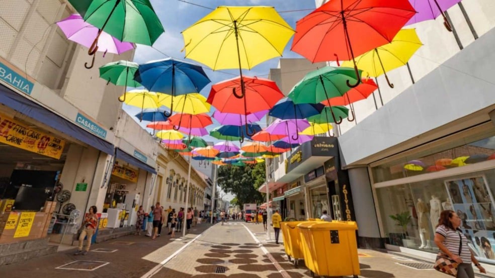 Rua do Centro de Jundiaí com lojas e pedestres, decorada com guarda-chuvas coloridos suspensos sobre a via. Rua do Centro de Jundiaí com lojas e pedestres, decorada com guarda-chuvas coloridos suspensos sobre a via.