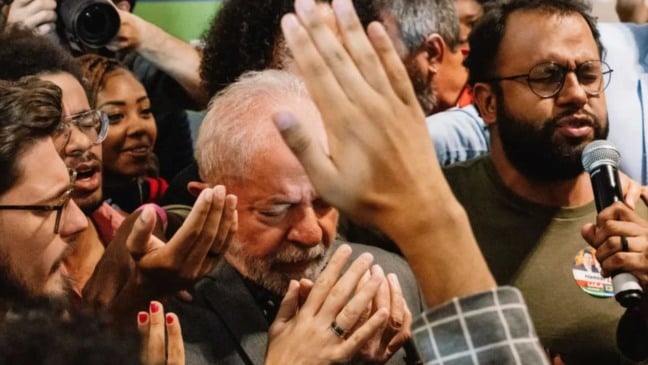 Presidente Lula participa de momento de oração coletiva, cercado por apoiadores com mãos erguidas durante encontro religioso.