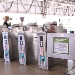 Catracas de acesso da estação da Linha 7-Rubi com passageiros circulando e agente de segurança uniformizada acompanhando o fluxo no interior da estação.