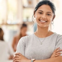 Jovem estudante sorridente, em ambiente de estudo ou trabalho colaborativo, representando oportunidade de est&aacute;gio e desenvolvimento profissional.
