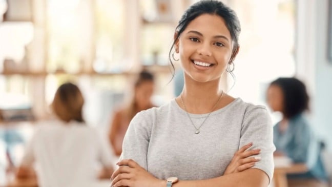 Jovem estudante sorridente, em ambiente de estudo ou trabalho colaborativo, representando oportunidade de estágio e desenvolvimento profissional.