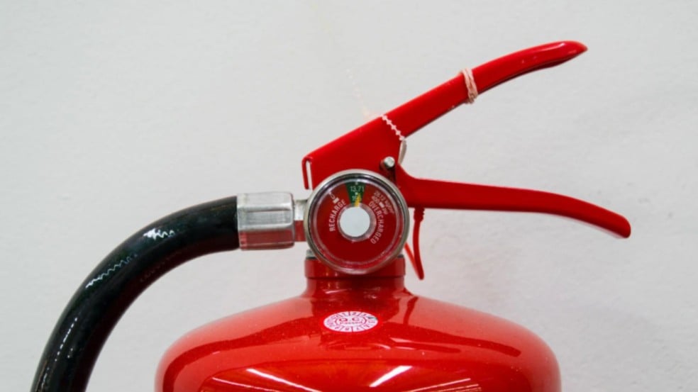 Extintor de incêndio vermelho com manômetro de pressão, gatilho e mangueira preta, fotografado em fundo claro. Extintor de incêndio vermelho com manômetro de pressão, gatilho e mangueira preta, fotografado em fundo claro.