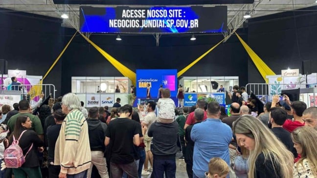 Público acompanha apresentação no palco da FENS, no Parque da Uva, em Jundiaí, com painel exibindo o site negocios.jundiai.sp.gov.br.