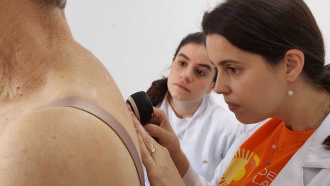 Médica realiza exame de pele com dermatoscópio em paciente durante campanha de prevenção ao câncer de pele.