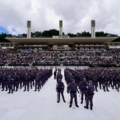 Panorama de um estádio com grande público nas arquibancadas e formação de centenas de policiais posicionados no centro durante cerimônia de formatura.