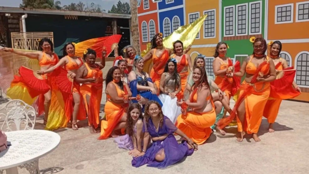 Grupo de bailarinas de dança do ventre posa sorrindo ao ar livre, com figurinos coloridos e leques, em cenário cultural decorado. Grupo de bailarinas de dança do ventre posa sorrindo ao ar livre, com figurinos coloridos e leques, em cenário cultural decorado.