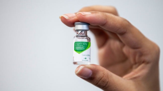 Mão segurando um frasco da vacina contra o HPV, com rótulo verde e branco em destaque.
