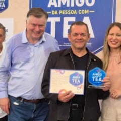 Grupo de seis pessoas posa sorrindo diante de um painel azul do Selo Amigo da Pessoa com TEA; ao centro, Edison Gonçalves segura o certificado e o troféu recebidos pela APAE de Jundiaí.