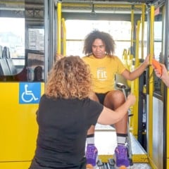 Pessoa participando de atividade de inclusão é erguida na plataforma elevatória de um ônibus acessível, acompanhada por dois orientadores no Terminal Vila Arens, em Jundiaí.