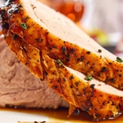 Fatias de lombo assado com crosta dourada e molho, em close.