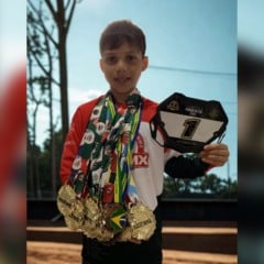 Lucca Bernardes, 7 anos, segura placa n&uacute;mero 1 e exibe v&aacute;rias medalhas de ouro no pesco&ccedil;o, posando com orgulho ap&oacute;s conquistas no BMX.