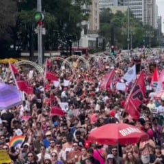 Multidão ocupa a Avenida Paulista durante a mobilização nacional “Mulheres Vivas”, com manifestantes segurando bandeiras, faixas e cartazes contra o feminicídio; prédios e decoração urbana aparecem ao fundo.