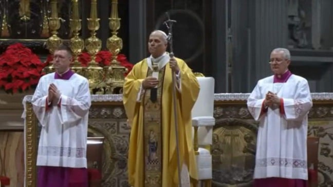 Papa Leão 14 celebra a Missa do Galo na Basílica de São Pedro, no Vaticano, usando vestes douradas e acompanhado por dois clérigos diante de um altar decorado com flores vermelhas e castiçais dourados.