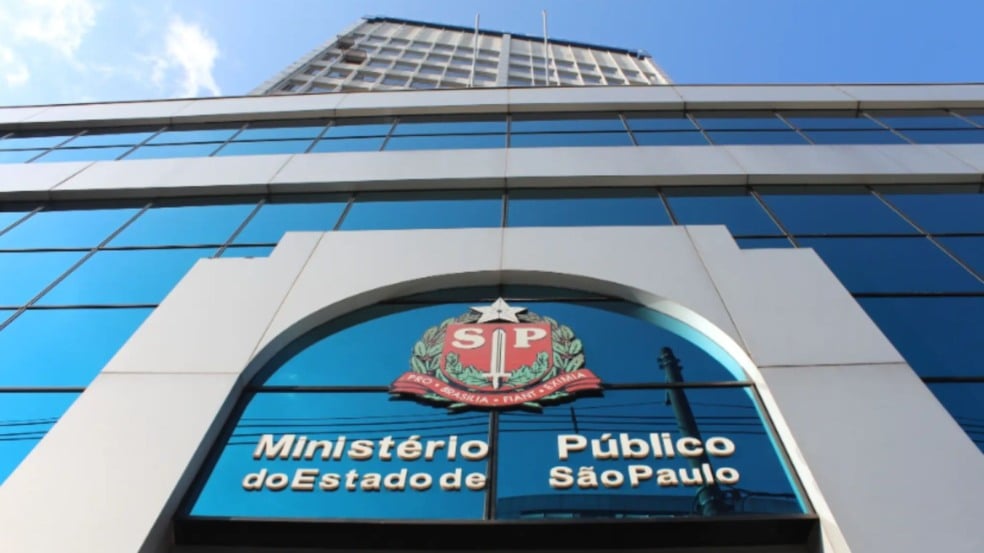 Fachada envidraçada do Ministério Público do Estado de São Paulo, com o brasão paulista ao centro refletido nos painéis azuis do prédio.