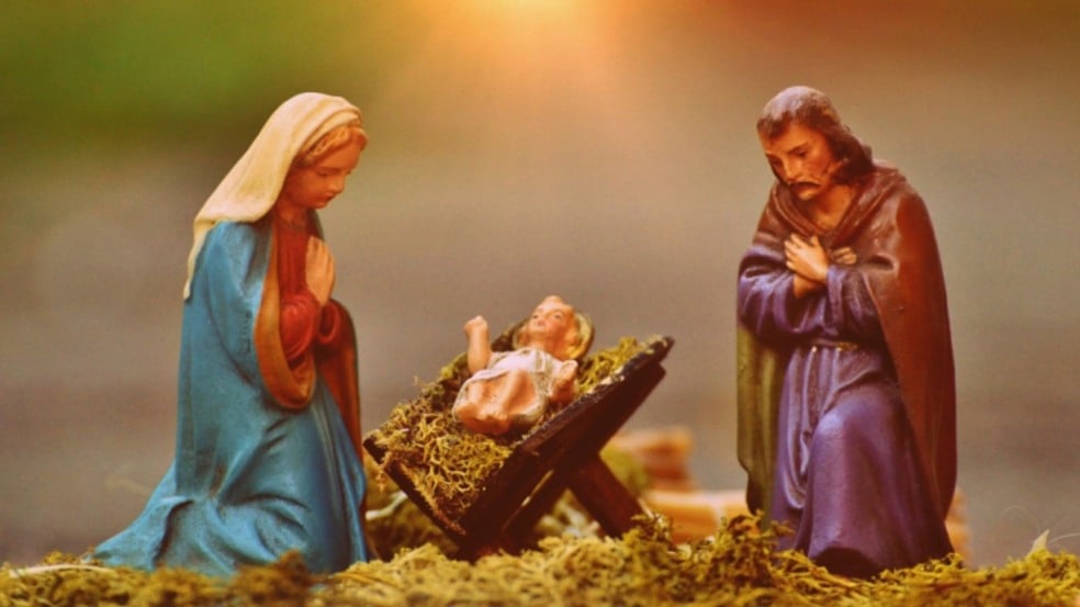 Presépio com figuras de Maria e José ajoelhados ao lado do Menino Jesus deitado em uma manjedoura, iluminados por um brilho dourado ao fundo. Presépio com figuras de Maria e José ajoelhados ao lado do Menino Jesus deitado em uma manjedoura, iluminados por um brilho dourado ao fundo.