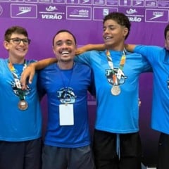 Atletas do Time Jundiaí e o técnico Marcelinho posando com medalhas em frente a painel roxo do campeonato.