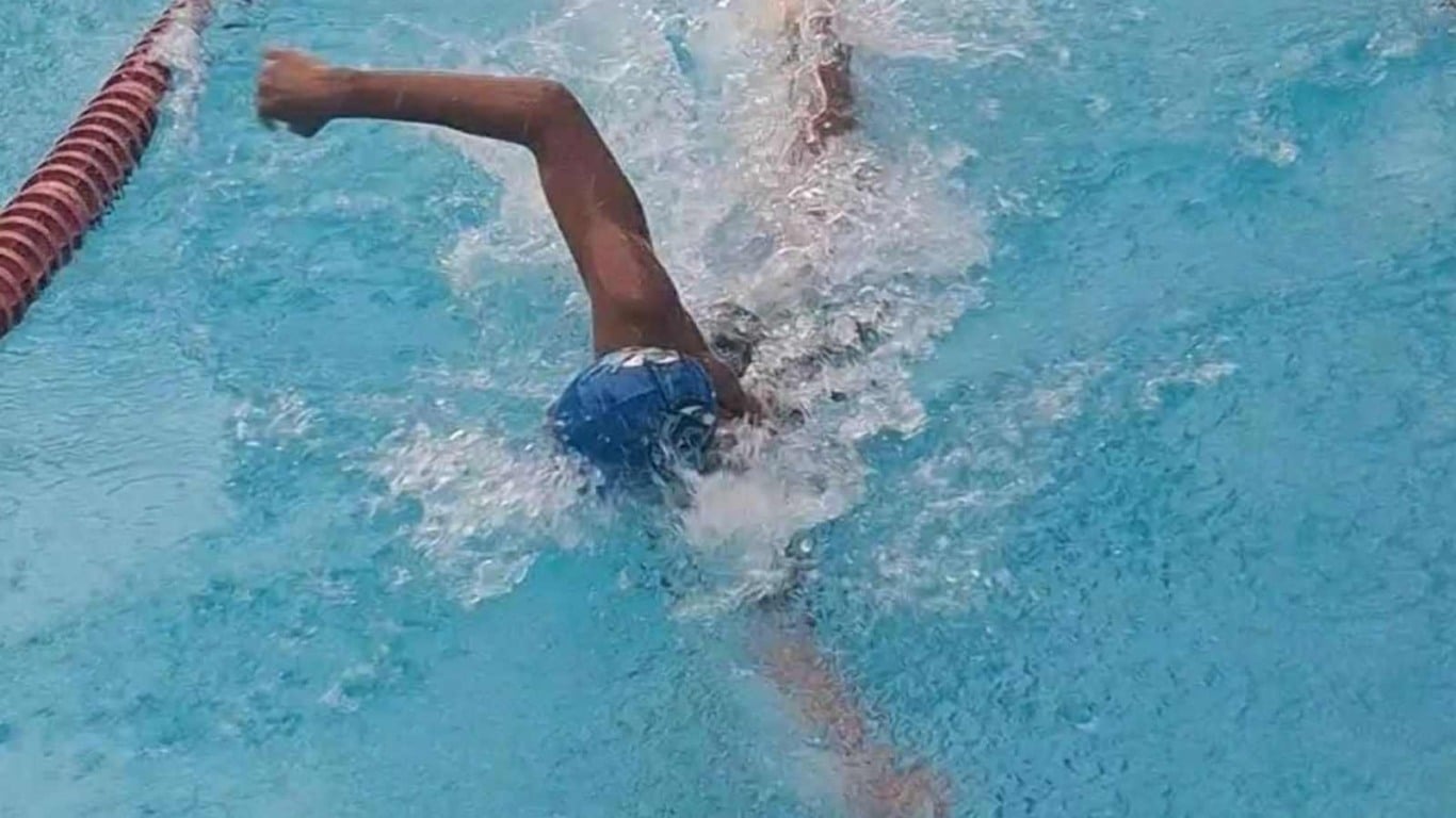 Nadador de touca azul executando nado livre em piscina, com água agitada e raia vermelha ao lado.