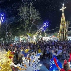 Multid&atilde;o acompanha desfile natalino sob neve artificial, com artistas fantasiados e uma grande &aacute;rvore de Natal iluminada ao fundo.