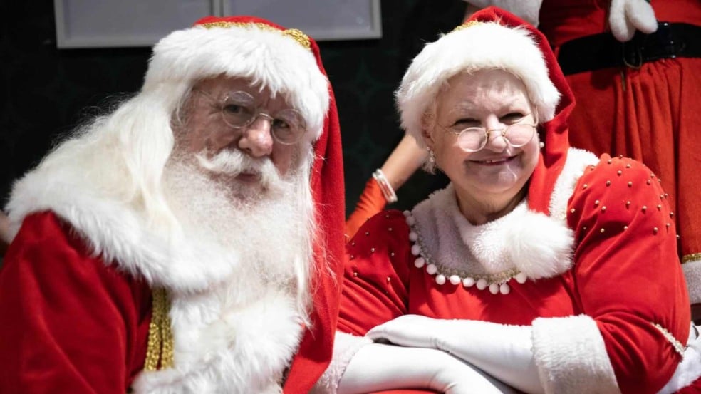 Papai Noel e Mamãe Noel sorrindo e vestidos com trajes tradicionais vermelhos e brancos, posando durante evento natalino. Papai Noel e Mamãe Noel sorrindo e vestidos com trajes tradicionais vermelhos e brancos, posando durante evento natalino.
