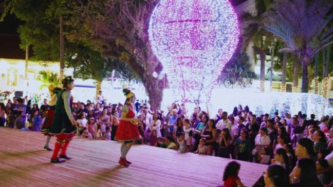 Artistas se apresentam em palco na Praça da Catedral durante o Natal Luz em Jundiaí, com grande público e balão iluminado ao fundo.