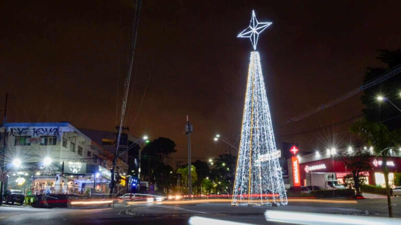 Árvore de Natal iluminada em Várzea Paulista instalada em uma rotatória, com estrela no topo e cidade ao fundo à noite.