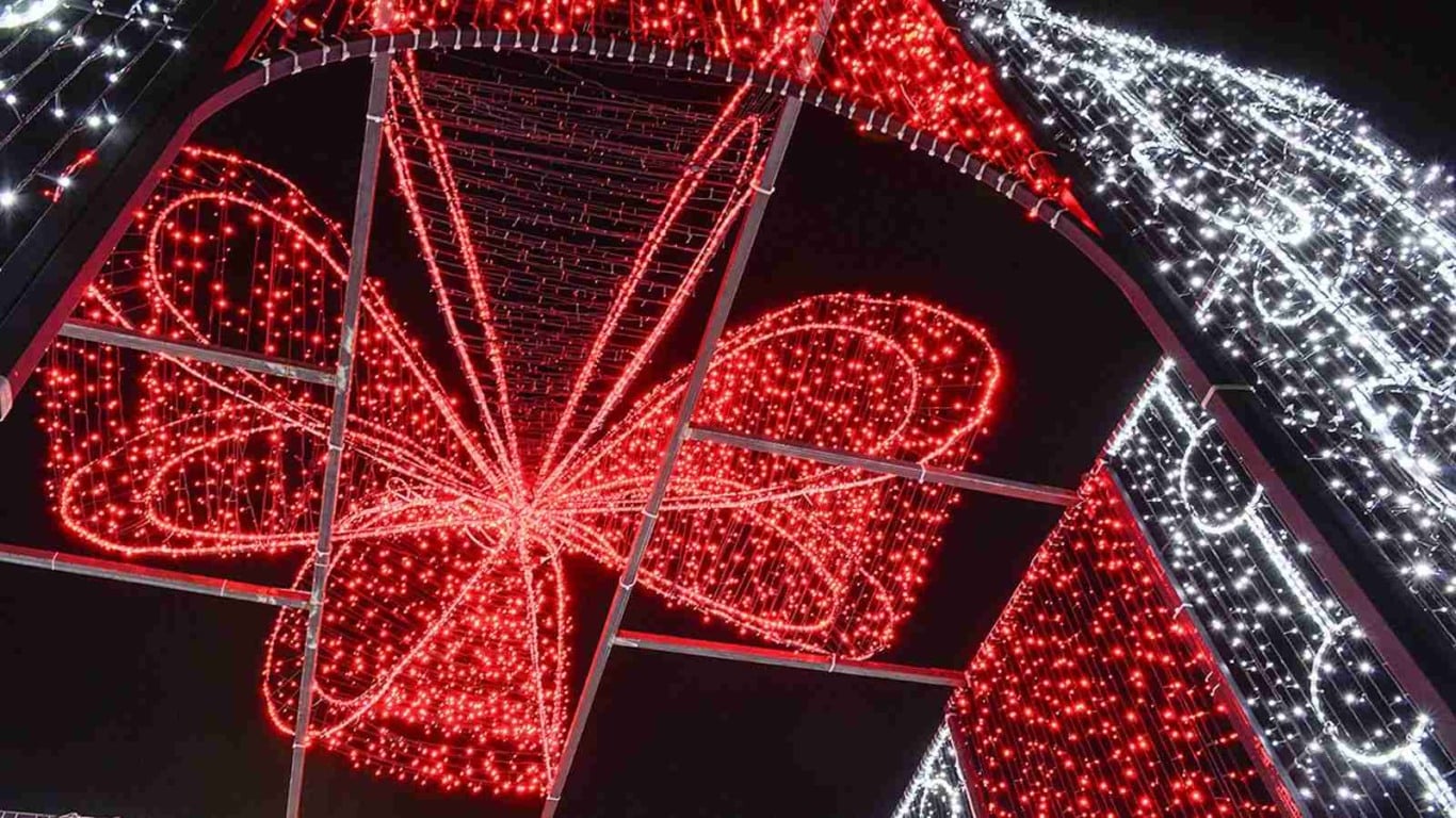 Presente natalino gigante iluminado com luzes vermelhas e brancas visto por dentro, com laço iluminado no topo.