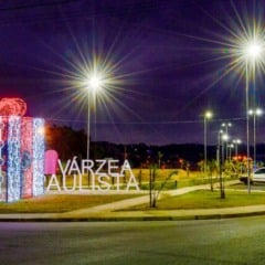 Presente natalino gigante iluminado no Parque da Família ao lado do letreiro “Várzea Paulista”, durante a noite.
