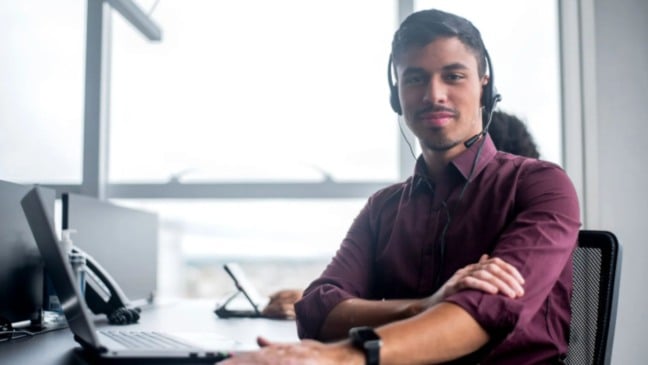 Profissional em escritório usando headset e computador, representando atuação em atendimento e análise no setor financeiro.