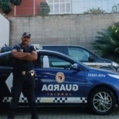 Dois guardas municipais uniformizados posam com os braços cruzados ao lado de uma viatura da Guarda Municipal de Jundiaí em área externa.
