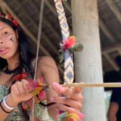 Crian&ccedil;a ind&iacute;gena com pintura facial segura arco e flecha durante viv&ecirc;ncia cultural ao ar livre no Sesc Jundia&iacute;.