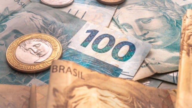 Notas e moedas do real brasileiro, com destaque para uma cédula de R$ 100, simbolizando pagamento de benefícios e valores financeiros.