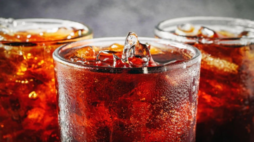 Copo de refrigerante escuro com gelo e condensação na superfície, em close, ao lado de outras bebidas semelhantes. Copo de refrigerante escuro com gelo e condensação na superfície, em close, ao lado de outras bebidas semelhantes.