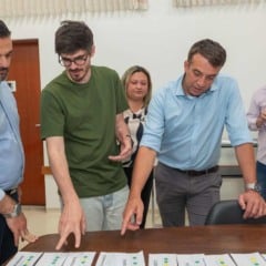 Prefeito Gustavo Martinelli e equipe analisam documentos sobre a mesa durante reuni&atilde;o de planejamento vi&aacute;rio.