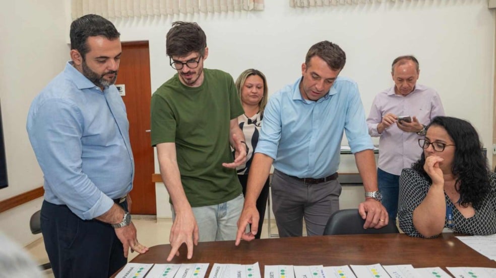 Prefeito Gustavo Martinelli e equipe analisam documentos sobre a mesa durante reunião de planejamento viário. Prefeito Gustavo Martinelli e equipe analisam documentos sobre a mesa durante reunião de planejamento viário.