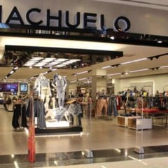 Fachada de loja da Riachuelo em shopping, com manequins, araras de roupas e ambiente interno amplo e bem iluminado.