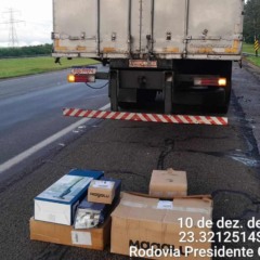 Caixas de mercadorias recuperadas posicionadas no acostamento da Rodovia Castello Branco, ao lado de um caminh&atilde;o, durante registro policial da ocorr&ecirc;ncia em 10 de dezembro de 2025.