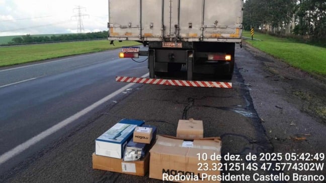 Caixas de mercadorias recuperadas posicionadas no acostamento da Rodovia Castello Branco, ao lado de um caminhão, durante registro policial da ocorrência em 10 de dezembro de 2025.