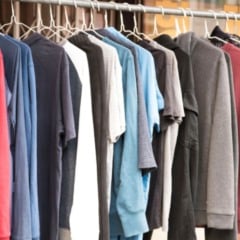 Arara com várias peças de roupa — camisetas e blusas de manga longa em diferentes cores — penduradas em cabides metálicos.
