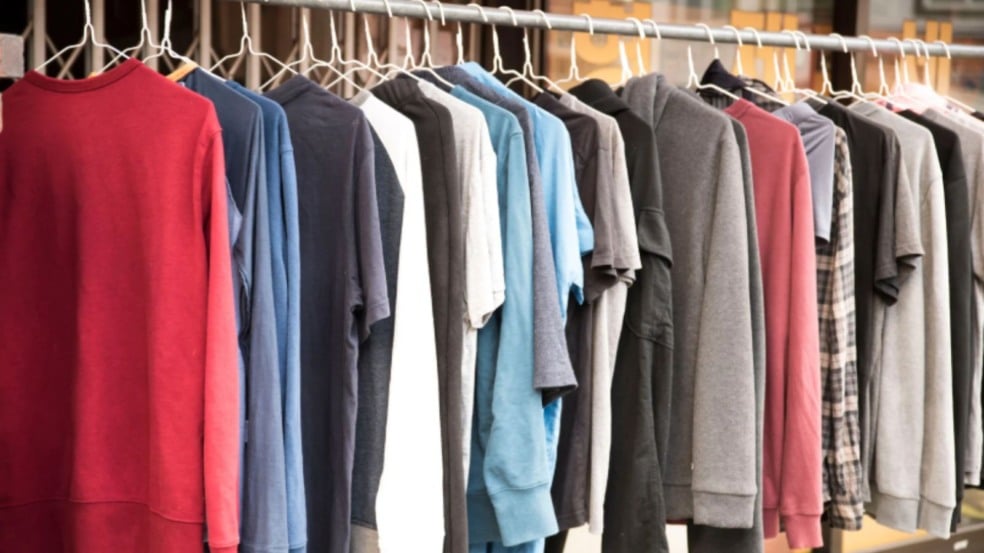 Arara com várias peças de roupa — camisetas e blusas de manga longa em diferentes cores — penduradas em cabides metálicos.