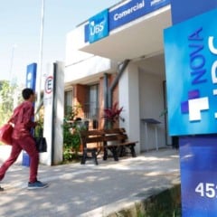 Fachada de uma Unidade B&aacute;sica de Sa&uacute;de de Jundia&iacute;, com totem azul &lsquo;Nova UBS&rsquo; em destaque e pessoas caminhando em dire&ccedil;&atilde;o &agrave; entrada.