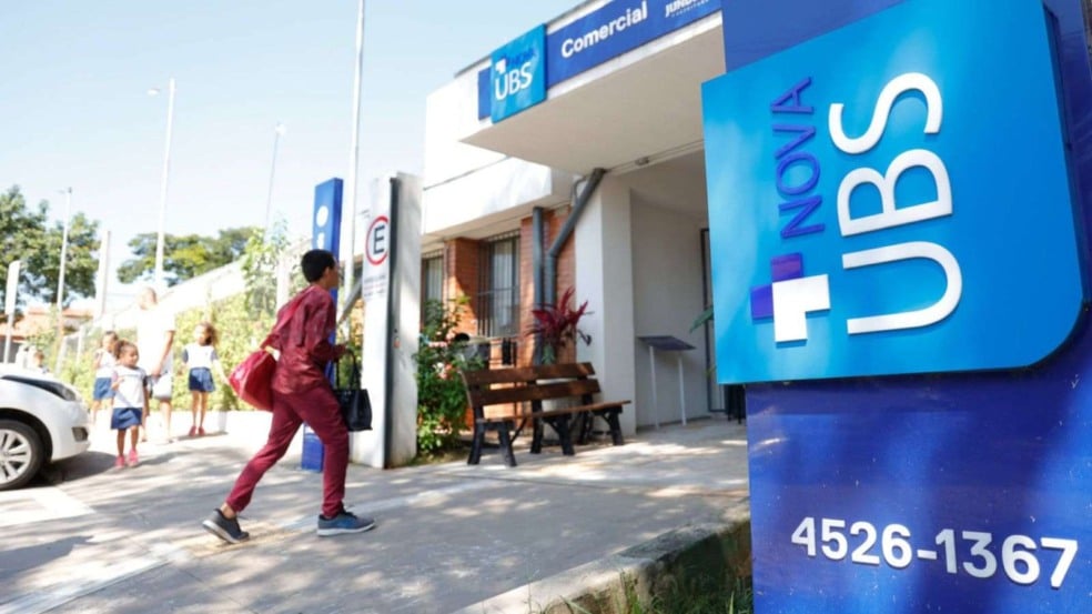 Fachada de uma Unidade Básica de Saúde de Jundiaí, com totem azul ‘Nova UBS’ em destaque e pessoas caminhando em direção à entrada. Fachada de uma Unidade Básica de Saúde de Jundiaí, com totem azul ‘Nova UBS’ em destaque e pessoas caminhando em direção à entrada.