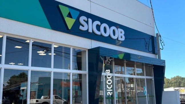 Fachada de agência do Sicoob Integrado com logotipo em azul e verde, prédio moderno com grandes janelas de vidro em área urbana.