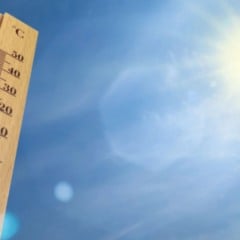 Termômetro de madeira indicando temperatura alta, com céu azul e sol forte ao fundo.