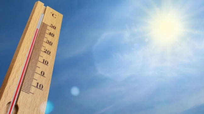 Termômetro de madeira indicando temperatura alta, com céu azul e sol forte ao fundo.
