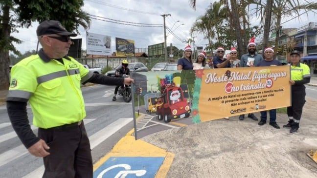 Agentes de trânsito de Várzea Paulista participam de blitz educativa com faixa de conscientização sobre segurança no trânsito durante o Natal, em via urbana.