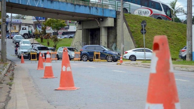 Cones e barreiras bloqueiam trecho de avenida sob viaduto, com carros parados em fila durante interdição para obras de saneamento em Várzea Paulista.