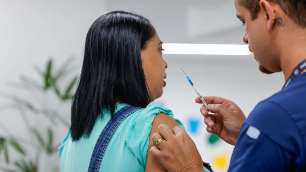 Profissional de saúde segurando uma seringa enquanto se prepara para aplicar vacina no braço de uma mulher em um ambiente de atendimento. Profissional de saúde segurando uma seringa enquanto se prepara para aplicar vacina no braço de uma mulher em um ambiente de atendimento.