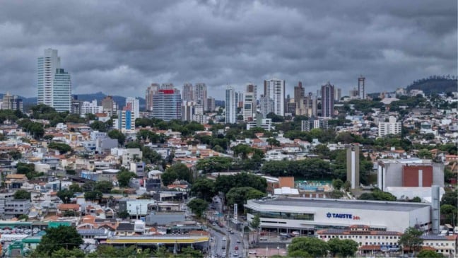 Cidade de Jundiaí vista de cima, com prédios e casas sob nuvens escuras e carregadas, indicando tempo instável e risco de ventos fortes.